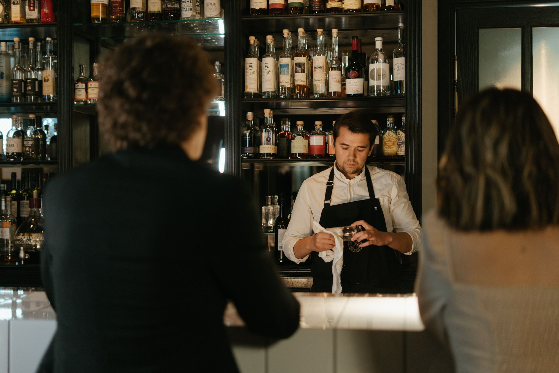 Bartender prepares drinks while guests sit at a stylish bar. — Photo by cottonbro studio on Pexels